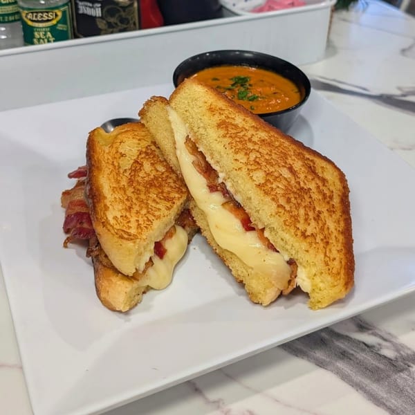 Grilled cheese with bacon, cut in half, served with a side of tomato soup.