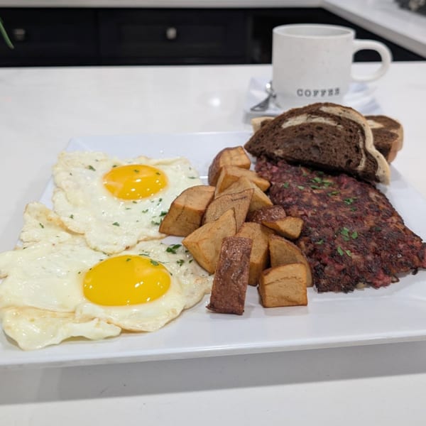 Breakfast plate with two fried eggs, home fries, corned beef hash, and marble rye toast.